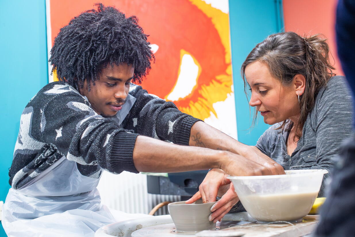 A young person learning pottery with a colleague at a foyer.