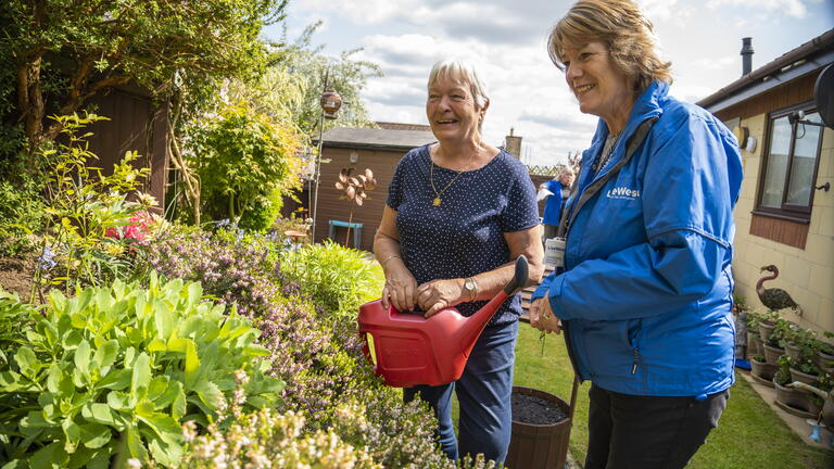 LiveWest colleague and a customer watering some plants in a garden using a watering can.