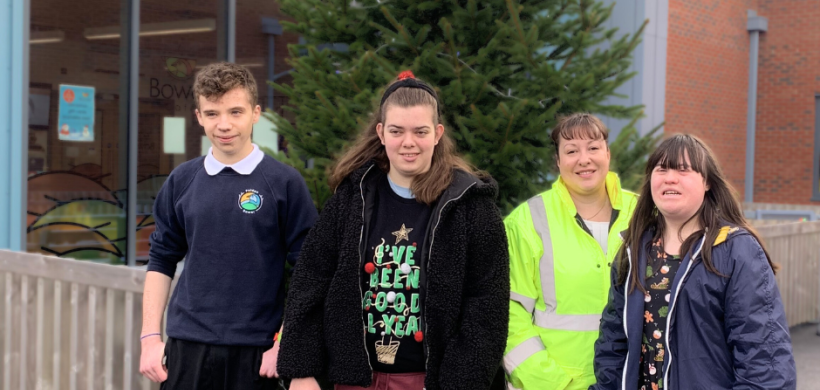 Local school students smiling in front of their new Christmas tree, donated by us.