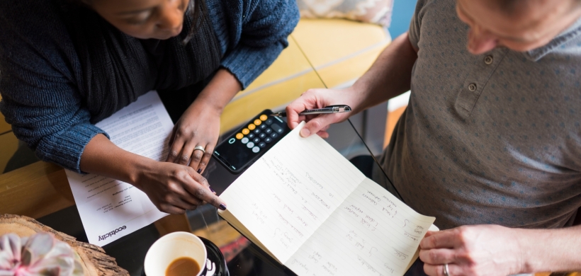 Two people sat at a desk looking at a notepad. 