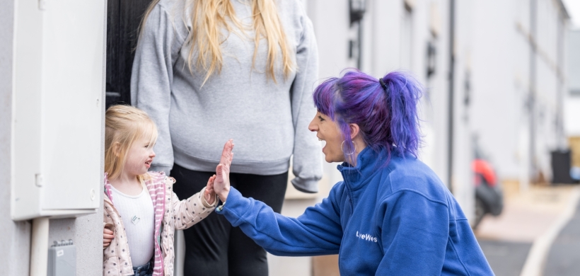 LiveWest colleague high fiving a child outside a house, with the mother standing next to the child. 