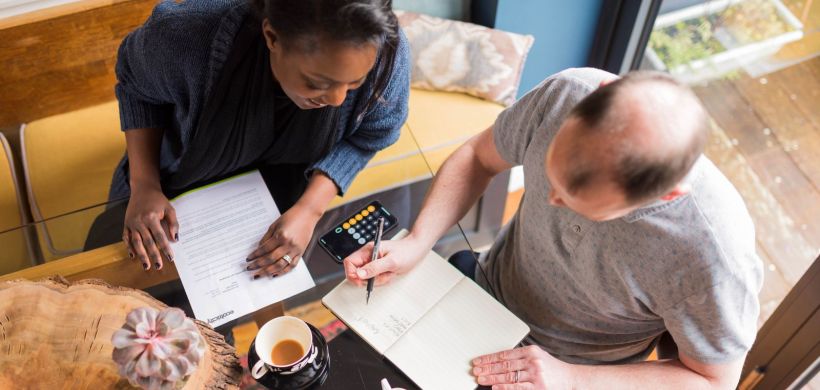 Two people sat at a table working out a budget with a calculator, pen and paper.