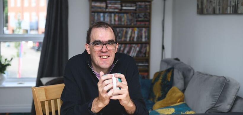Iain sat at his table drinking a hot drink in his new flat.