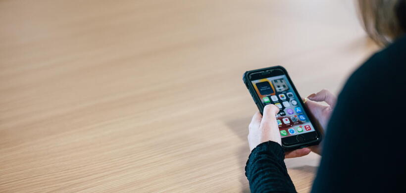 A person is holding and using a smartphone while sitting at a wooden table.