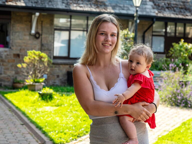 Samara holding Rozie-Mae and smiling at the camera.