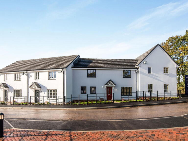 Modern semi-detached houses with white walls, black windows, and a red front door on a sunny day.