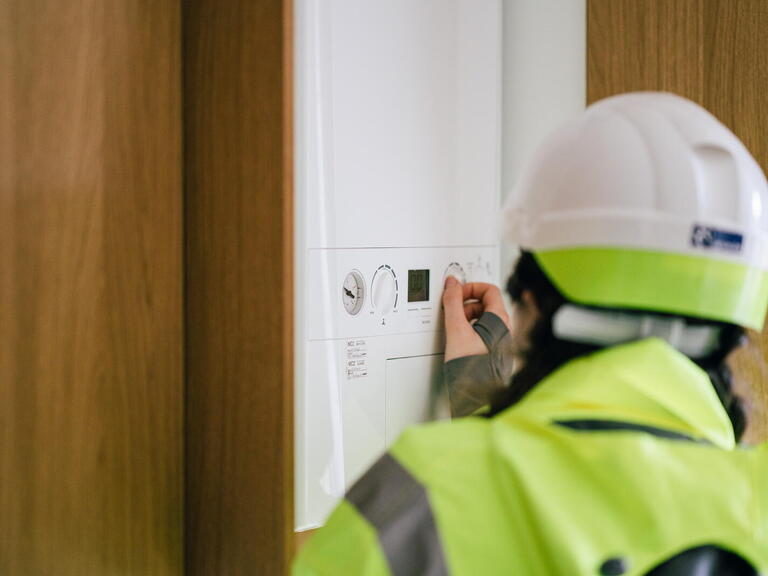 Image of someone wearing a hard hat and a bright yellow jacket adjusting a boiler. 