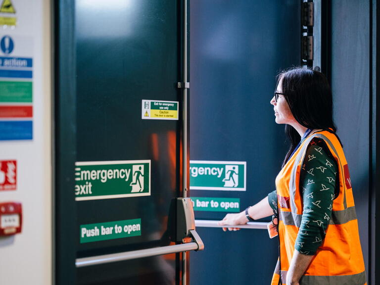 A person wearing a safety vest is opening an emergency exit door in a building.