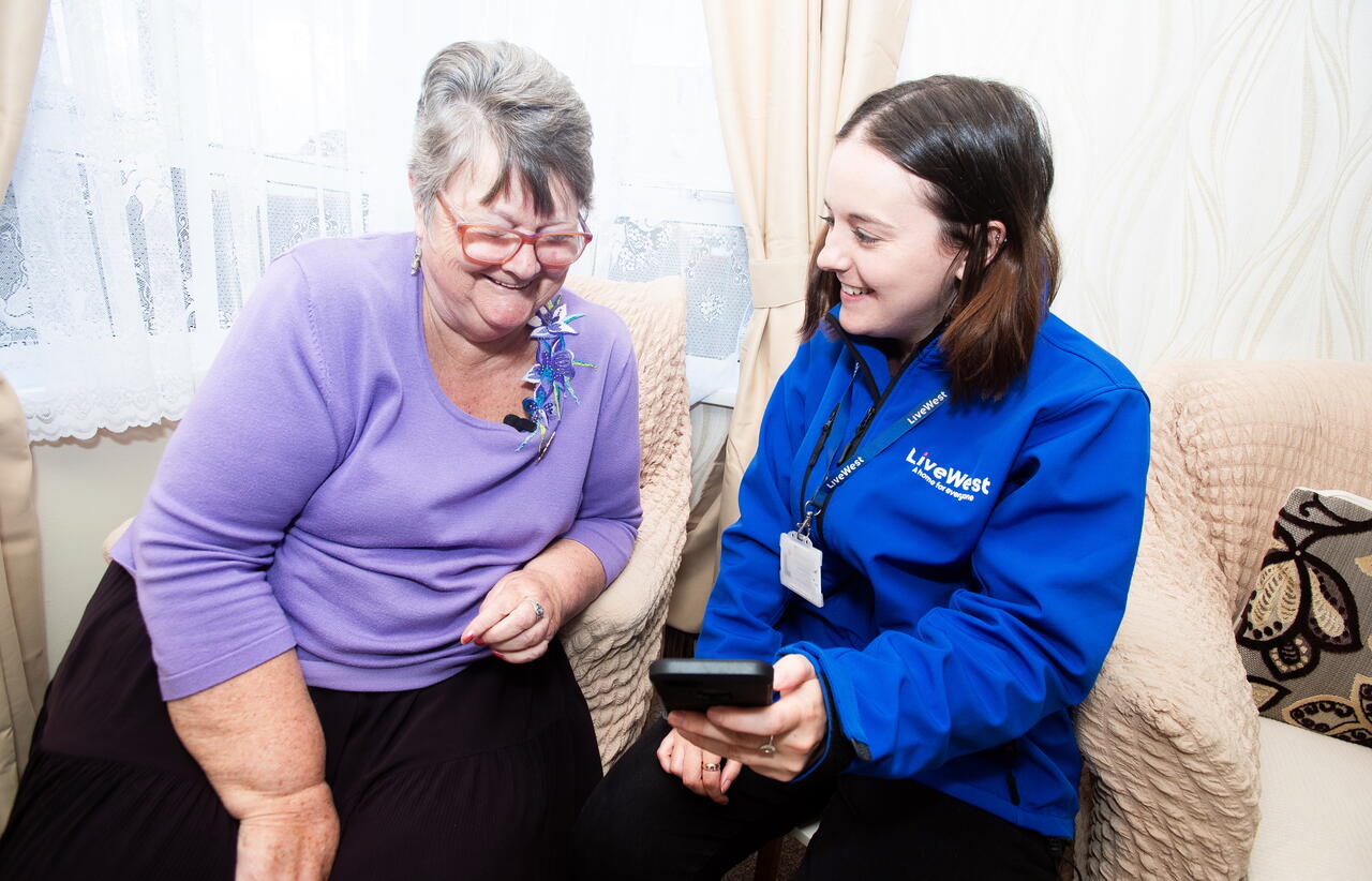 Image of a LiveWest colleague showing a customer how to use the portal on a mobile phone.