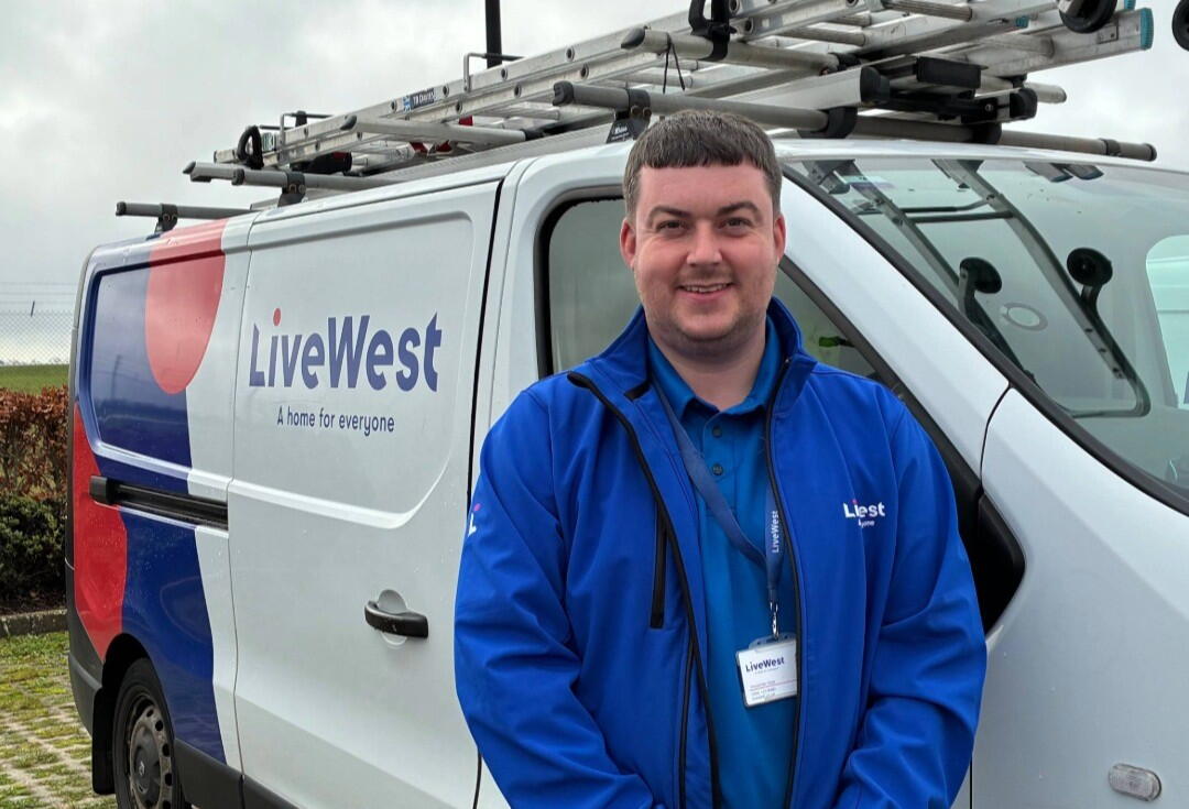Image shows Apprentice, Alex, stood smiling in front of a LiveWest van