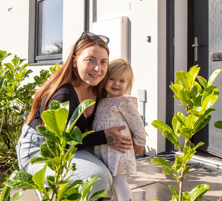 A woman and her daughter are smiling in front of their home.