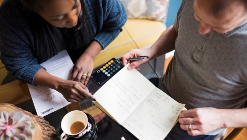 Two people sat at a desk looking at a notepad. 